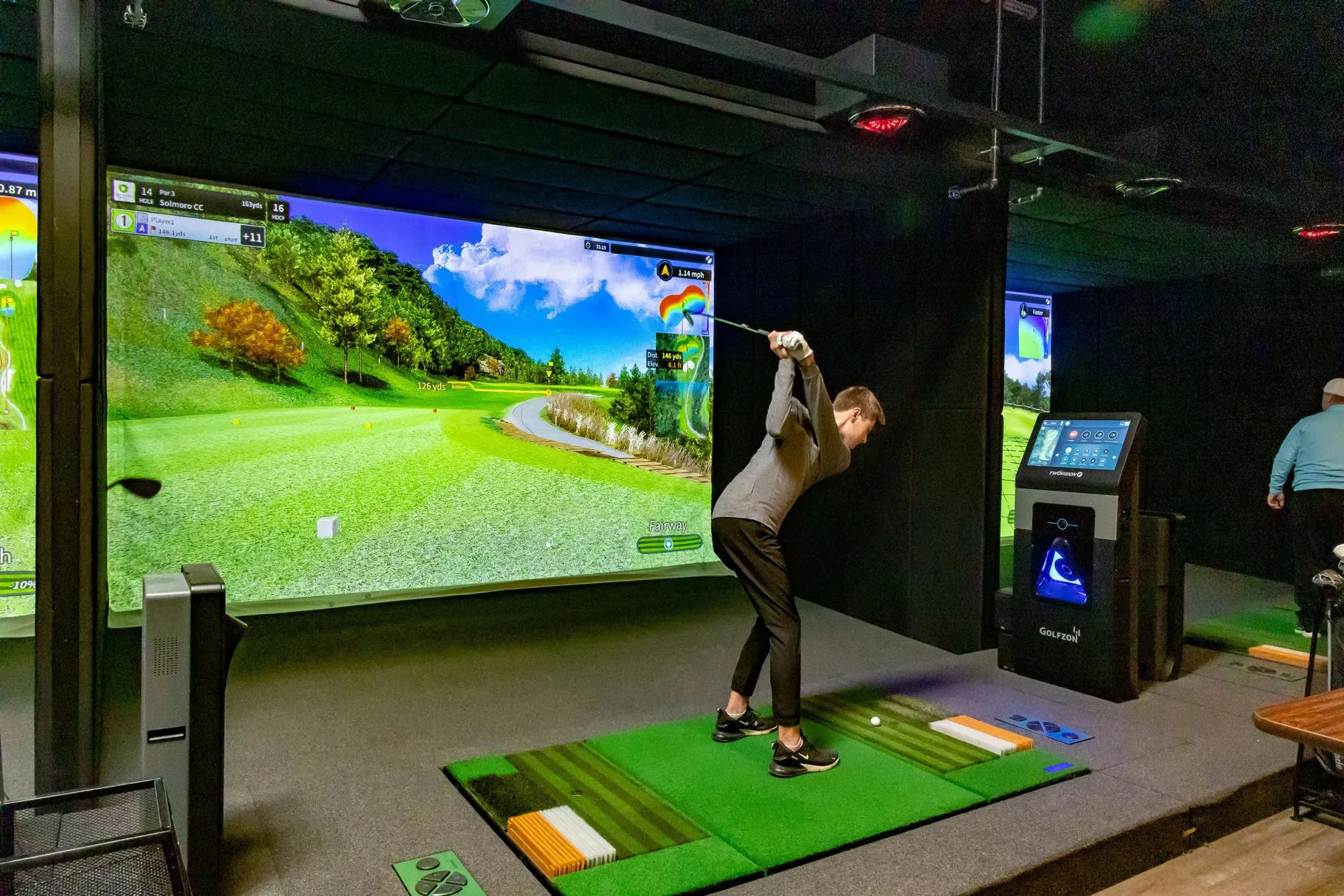 A golfer mid-swing in a simulator bay at The Links